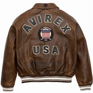 May include: A brown leather bomber jacket featuring the text AVIREX in black and white lettering across the upper back. Below this, a circular patch displays the text ALL AMERICANS ESTABLISHED 1975 with a US flag. The word USA is printed below.