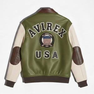 Op de afbeelding: Een olijfgroen varsity-jack met cr&egrave;mekleurige mouwen, bruine leren elleboogstukken en een bruine kraag en zoom. Op de achterkant staat de tekst AVIREX en USA in zwarte letters, samen met een ronde badge met een afbeelding van een Amerikaanse vlag.