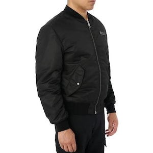 K&ouml;nnte beinhalten: Schwarze Bomberjacke mit geripptem Kragen, B&uuml;ndchen und Saum. Die Jacke hat einen Frontrei&szlig;verschluss, eine einzelne Tasche mit Druckknopfverschluss und einen kleinen Logoaufn&auml;her auf der Brust. Die Jacke ist aus glattem, gl&auml;nzendem Material.