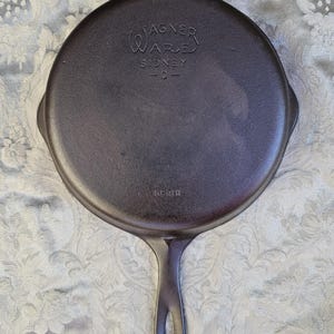 May include: A round black cast iron skillet with a handle featuring a hole at the end. The underside is embossed with the text WAGNER WARE SIDNEY -O- and the number 1058H. The surface has a dark, matte finish with visible metallic texture.