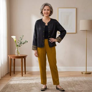 May include: A black long-sleeved jacket with a mandarin collar, gold-toned toggle closures, and gold embroidered cuffs, worn over a black top and mustard yellow trousers with a high waist and a straight-leg cut, paired with black flat shoes.