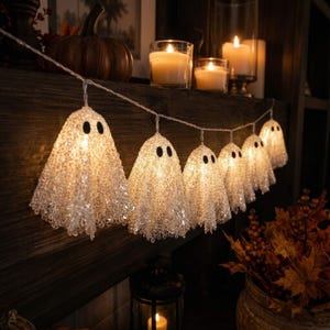 May include: A string of decorative LED lights featuring multiple ghost-shaped covers. Each ghost is constructed from a translucent, textured material that glows from within, accented with two small black oval eyes. The lights are connected by a thin wire.