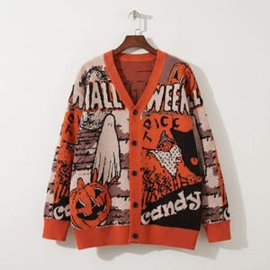 Könnte beinhalten: Eine orange-schwarze Strickjacke mit V-Ausschnitt, langen Ärmeln und fünf dunklen Knöpfen. Das Kleidungsstück zeigt ein grafisches Muster aus Kürbissen, Geistern sowie den Schriftzug "HALLOWEEN" und "candy" auf der Vorderseite und den Ärmeln.
