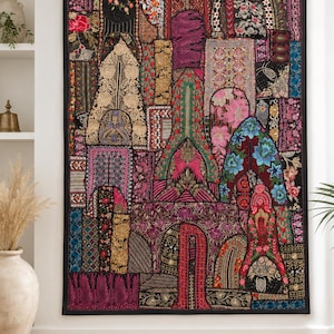 Könnte beinhalten: Ein rechteckiger Wandbehang aus einem Patchwork bestickter Stoffbahnen in Schwarz, Pink, Rot, Blau und Gold. Das Design umfasst komplexe florale Motive, geometrische Muster und bogenförmige architektonische Elemente mit detaillierten Stickereien.