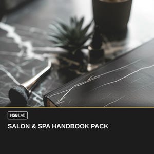 Pode incluir: Um manual com um padrão de mármore preto e branco com o texto "SALON & SPA HANDBOOK PACK" é exibido em uma superfície de mármore. Uma escova de maquiagem e uma pequena planta em vaso também são visíveis. O manual tem uma borda dourada.