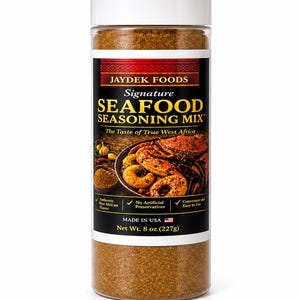 May include: A clear plastic bottle of Jaydek Foods Signature Seafood Seasoning Mix. The label features the text "SEAFOOD SEASONING MIX" and "The Taste of True West Africa." The bottle contains a brown spice blend and is marked as 8 oz (227g).