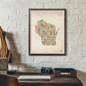 Puede incluir: Una impresión enmarcada de un mapa de estilo vintage de Wisconsin, creado utilizando los nombres de las ciudades y pueblos del estado. El mapa está impreso en un fondo beige con una textura desgastada. El texto está en varios colores, incluyendo rojo, azul, verde y amarillo.