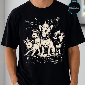 May include: A black t-shirt featuring a cream-colored graphic print of three dogs with spiked mohawk hairstyles and spiked collars. The dogs are depicted in a stylized, distressed illustration style. The text PrintoraCore appears in a small circle.
