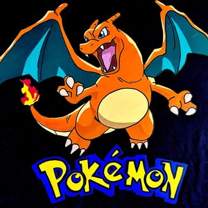 Puede incluir: Ilustración de Charizard naranja con alas azules y una llama en la cola, sobre un fondo negro. El logotipo de Pokémon se muestra en amarillo y azul debajo del personaje.