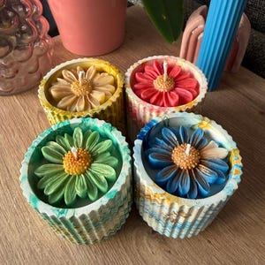 Peut inclure: Quatre bougies cylindriques dans des contenants texturés et marbrés, chacune surmontée d'une fleur en cire. Les bougies comprennent une fleur jaune dans un pot jaune, une fleur rouge dans un pot marbré rose, une fleur verte dans un pot marbré vert et une fleur bleue dans un pot marbré bleu.