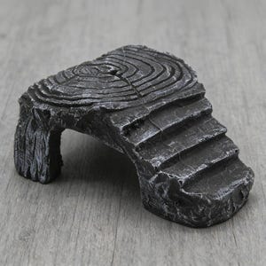 May include: A dark gray, textured resin aquarium decoration. The piece resembles a weathered log with a staircase and an archway. The top surface has concentric circle details, mimicking tree rings. The overall design is a naturalistic, miniature landscape.