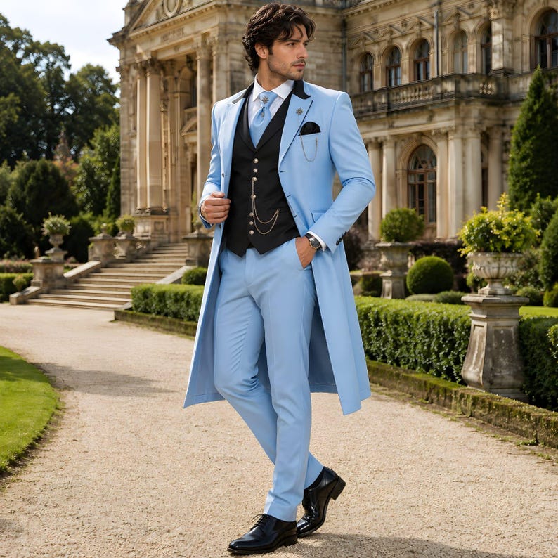 May include: A light blue suit with a long coat, black vest, and matching pants. The suit features a black pocket square and a silver chain. The person is wearing a white shirt and a light blue tie. Black leather shoes complete the outfit.