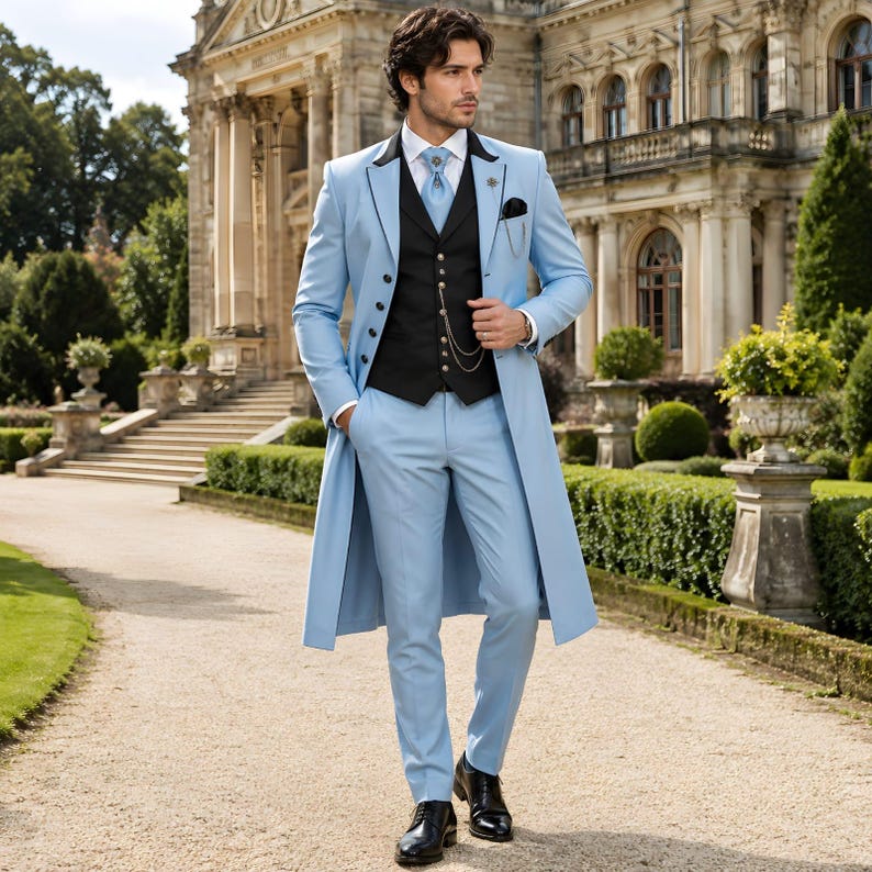 May include: A light blue suit with a long coat, black vest, and black shoes. The suit includes a matching tie and pocket square. The man is standing on a stone path in front of a large building.
