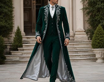 May include: A dark green velvet long coat featuring intricate silver floral embroidery along the lapels and cuffs, worn over a matching green vest and trousers with a white button-down shirt and a silver brooch, finished with a light gray lining.