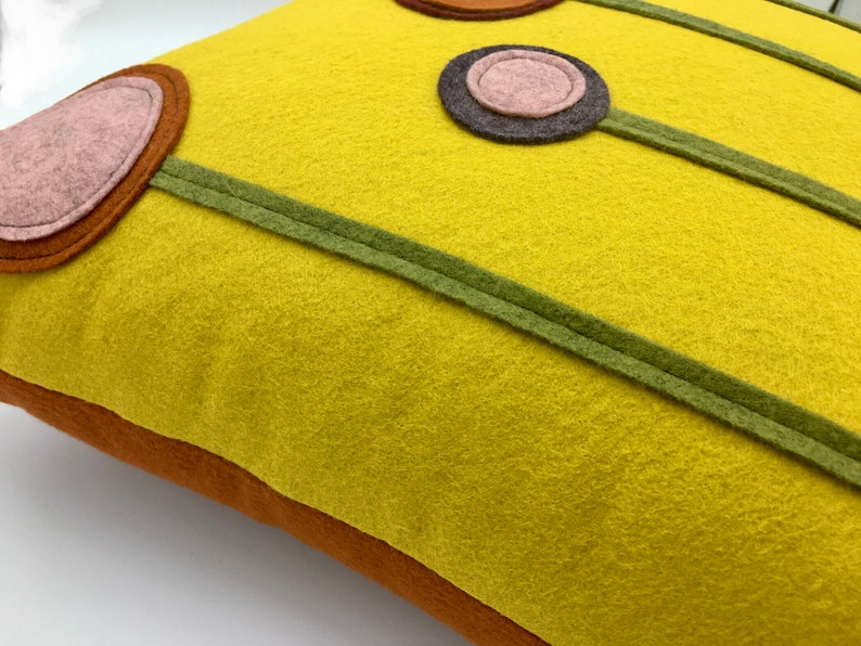 K&ouml;nnte beinhalten: Ein gelbes Kissen mit geometrischem Muster aus braunen, rosa und gr&uuml;nen Kreisen und Linien.