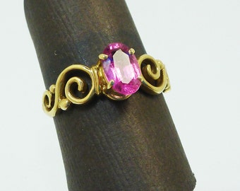 Puede incluir: Un anillo de oro con una piedra ovalada rosa engastada en un diseño de espiral.