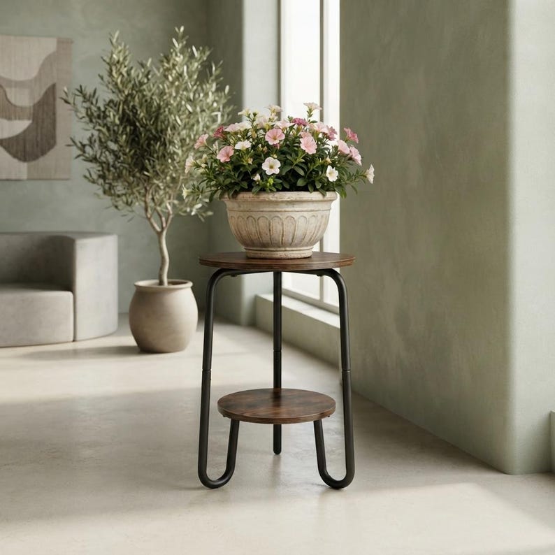 Pu&ograve; includere: Un portapiante a due livelli con un piano superiore in legno marrone scuro e un ripiano inferiore abbinato, sostenuto da una struttura in metallo nero con gambe a U. Un vaso in ceramica beige con fiori rosa e bianchi poggia sul ripiano.