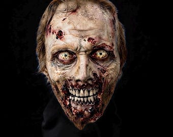 Puede incluir: Una máscara de zombi realista que presenta piel pálida y en descomposición con heridas, llagas y manchas de sangre visibles. La máscara tiene ojos hundidos y amarillentos, una sonrisa amplia y dentada con encías expuestas y cabello castaño claro ralo en la parte superior de la cabeza.