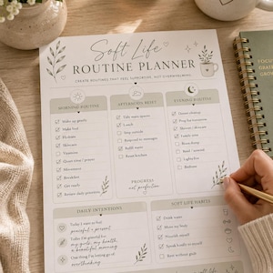 May include: A Soft Life Routine Planner with sections for morning, afternoon, and evening routines, daily intentions, and soft life habits. The planner includes checkboxes and prompts for self-care activities. A hand is holding a gold pen, ready to write.