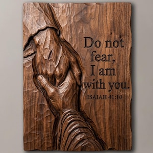 May include: A rectangular dark brown wooden wall plaque featuring a relief carving of two hands holding each other. The text "Do not fear, I am with you. ISAIAH 41:10" is engraved on the right side of the wood, which has a visible grain and texture.