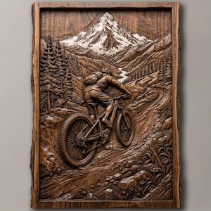 May include: A rectangular dark wood wall carving featuring a detailed relief of a mountain biker riding on a dirt trail. The scene includes a snow-capped mountain peak in the background, pine trees, and rocky terrain, all framed by a natural wood border.