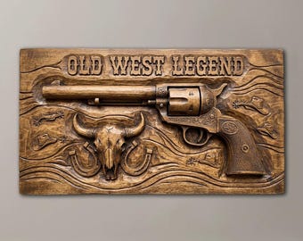 May include: A rectangular wooden wall plaque featuring a carved revolver, a steer skull, and horseshoes. The text OLD WEST LEGEND is carved across the top. The wood has a medium brown finish with visible grain patterns and carved western motifs.