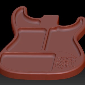 May include: A brown, guitar-shaped tray with three recessed compartments. The tray features a smooth, molded surface with the embossed text "ROCK & ROLL" located in the lower right section, following the contour of the guitar body shape.