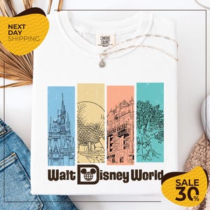 a white t-shirt with a graphic design depicting various landmarks and buildings from Walt Disney World, including the Eiffel Tower, the castle, and the roller coaster. The t-shirt is displayed on a white background, and there are yellow and black sale tags indicating a 30% discount.