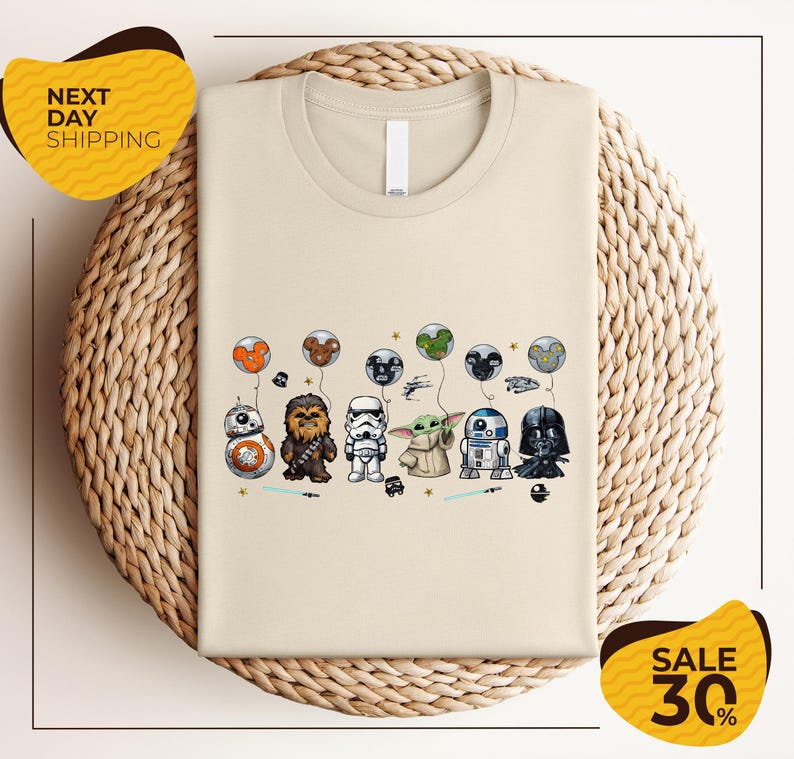 a beige t-shirt with a graphic design of various Star Wars characters, including Chewbacca, Stormtrooper, Darth Vader, and Baby Yoda, along with other Star Wars-themed elements.