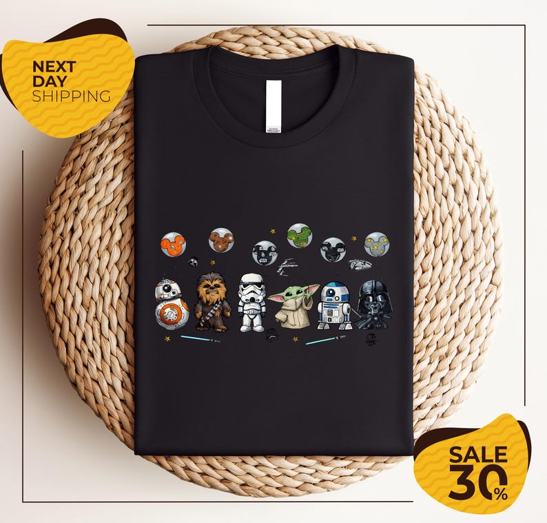 a black t-shirt with a graphic design of various Star Wars characters, including the main characters from the Star Wars franchise, such as Rey, Finn, and Chewbacca, along with other iconic characters like Bond, Baby Yoda, and Darth Vader. The t-shirt is displayed on a woven placemat, and there are two yellow sale signs in the image, indicating a discount or sale event.