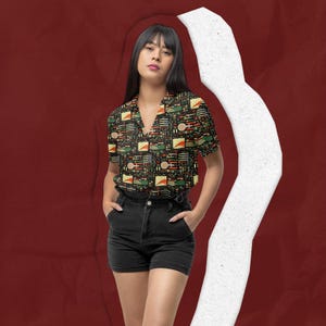 May include: A short-sleeved button-down shirt featuring a black base with a repeating geometric pattern in red, yellow, and green, paired with black denim shorts. The shirt has a notched collar and a straight hemline, while the shorts are high-waisted.