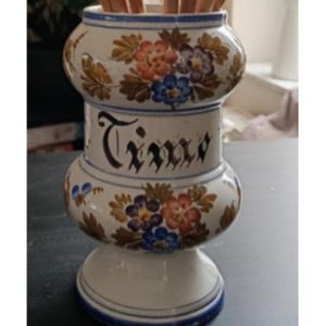May include: A white ceramic container with a floral design in red, blue, and orange. The word "Time" is written in black script on the center section. The container has a blue rim and base.