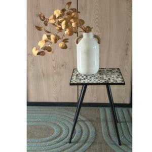 Könnte beinhalten: Eine weiße Keramikvase mit Seilgriffen enthält goldfarbene Zierzweige. Die Vase steht auf einem kleinen quadratischen Beistelltisch mit einer Mosaikfliesenplatte und schwarzen Metallbeinen. Der Tisch steht auf einem gemusterten Teppich.