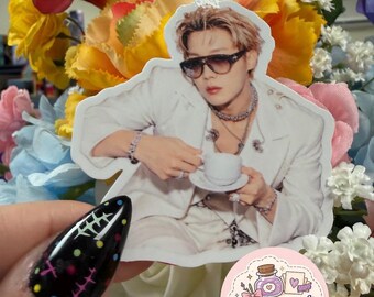 May include: A die-cut sticker featuring a person with light brown hair wearing dark sunglasses, a white blazer, and layered necklaces, holding a small white teacup and saucer. A circular logo with the text ApotheCraft Studio is visible.