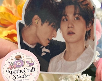 May include: A die-cut sticker featuring a photographic image of two individuals with dark hair, one leaning toward the other, accompanied by a smaller circular sticker with the text ApotheCraft Studio Crafted with a Dose of Joy.