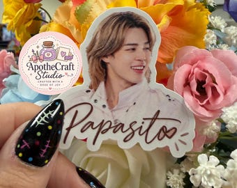 May include: A die-cut sticker featuring a portrait of a person with light brown hair and the word Papasito written in a dark brown script font. A circular logo for ApotheCraft Studio Crafted with a Dose of Joy is visible on the left side.