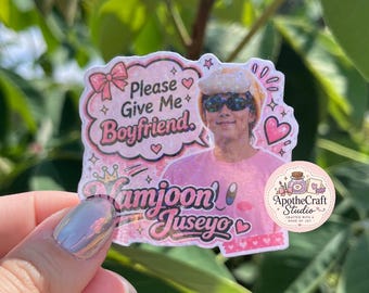 May include: A die-cut sticker featuring a person wearing a pink shirt, sunglasses, and a fuzzy hat, with text that reads Please Give Me Boyfriend, Namjoon, and Juseyo, surrounded by pink hearts, stars, and a small circular logo for ApotheCraft Studio.