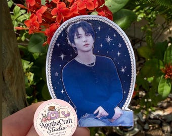 May include: A die-cut sticker featuring a portrait of a person with dark hair wearing a dark blue long-sleeved shirt against a dark blue background with white stars and a pearl-like border. A small round sticker with the text ApotheCraft Studio is visible.