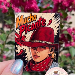 May include: A rectangular sticker featuring a stylized illustration of a person wearing a red cowboy hat and a red bandana. The text Mucho Picante is printed in bold letters at the top, accompanied by two red chili pepper graphics on a beige background.