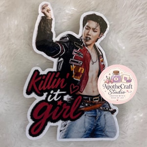 Puede incluir: Una pegatina troquelada que muestra a una persona de pelo oscuro con una chaqueta de cuero roja y negra abierta, una cadena plateada y vaqueros azules. El texto "Killin' it girl" aparece en letras rojas y negras junto a la figura, con un corazón.