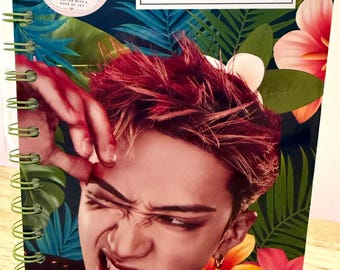 May include: A spiral-bound notebook featuring a tropical floral background with green palm leaves and pink and yellow hibiscus flowers. The cover displays a portrait of a person with reddish-brown hair and a sticker labeled ApotheCraft Studio.