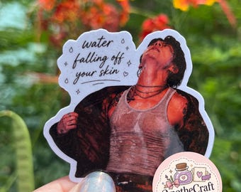 May include: A die-cut sticker featuring a person with dark hair looking upward, wearing a wet white tank top and a dark open shirt. The text "water falling off your skin" is printed in black script above the figure, accompanied by small star and heart icons.