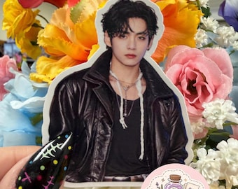 May include: A die-cut sticker featuring a portrait of a person with dark wavy hair wearing a black leather jacket over a black shirt with layered necklaces. A small circular logo with the text ApotheCraft Studio Crafted with a dose of joy.