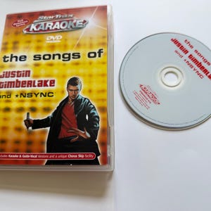 May include: A StarTrax Karaoke DVD case and disc featuring the songs of Justin Timberlake and *NSYNC. The cover displays a person in a black jacket and red shirt, with yellow background text. The disc is silver with red text and the StarTrax logo.