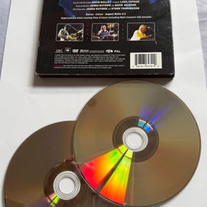 May include: A DVD case and two CDs from Pink Floyd's "Pulse" concert. The case is black with white text and images. The CDs are brown with reflective rainbow colors. The text on the case includes song titles and credits.