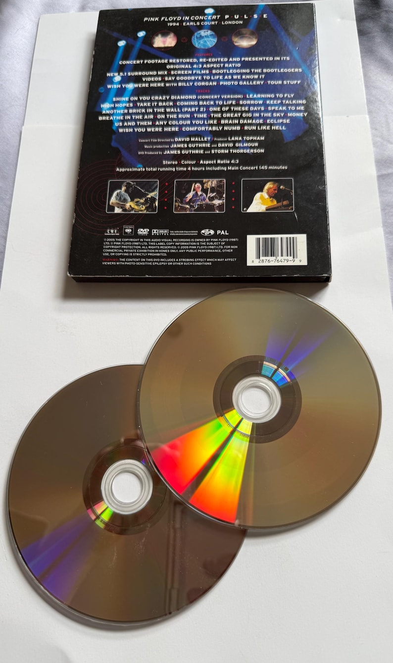 May include: A DVD case and two CDs from Pink Floyd's "Pulse" concert. The case is black with white text and images. The CDs are brown with reflective rainbow colors. The text on the case includes song titles and credits.