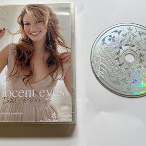 K&ouml;nnte beinhalten: Eine DVD-H&uuml;lle und eine Disc f&uuml;r Innocent Eyes von Delta Goodrem. Die H&uuml;lle zeigt eine l&auml;chelnde Person in einem hellen Oberteil mit dem Text Innocent Eyes und Delta Goodrem. Die silberne Disc hat ein wei&szlig;es, filigranes Blumenmuster und DVD-Logo.