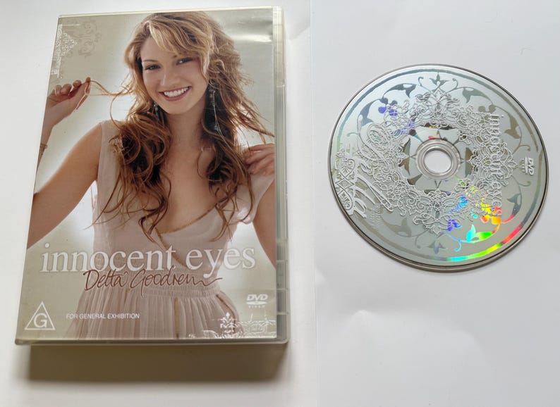 K&ouml;nnte beinhalten: Eine DVD-H&uuml;lle und eine Disc f&uuml;r Innocent Eyes von Delta Goodrem. Die H&uuml;lle zeigt eine l&auml;chelnde Person in einem hellen Oberteil mit dem Text Innocent Eyes und Delta Goodrem. Die silberne Disc hat ein wei&szlig;es, filigranes Blumenmuster und DVD-Logo.