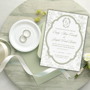 May include: A rectangular wedding invitation card with sage green accents and floral patterns, featuring the text Emily Anne Cassidy and Joseph Scott Ricker, August 2025, at The Dogana Estate in Florence, Italy, alongside two silver rings and ribbon.