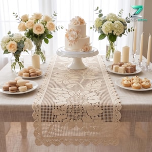May include: A beige crochet table runner with a floral pattern and scalloped edges, displayed on a table set with a two-tier cake on a white stand, vases of cream and white flowers, plates of macarons and small pastries, and several pillar candles.
